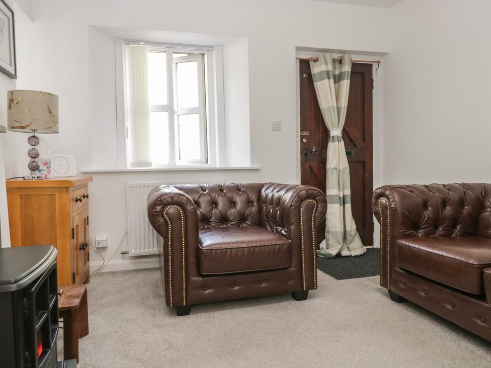 A living room with brown armchairs and a wooden cabinet at Fellfoot Cottage