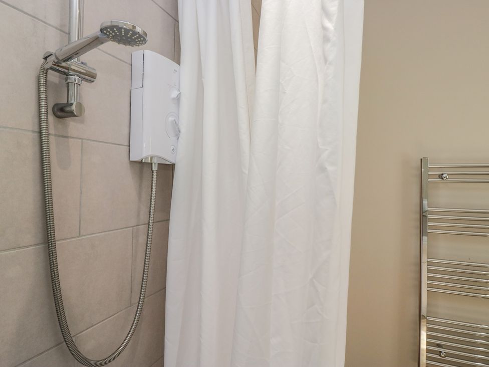 A shower with a curtain and heating towel rail at Fellfoot Cottage