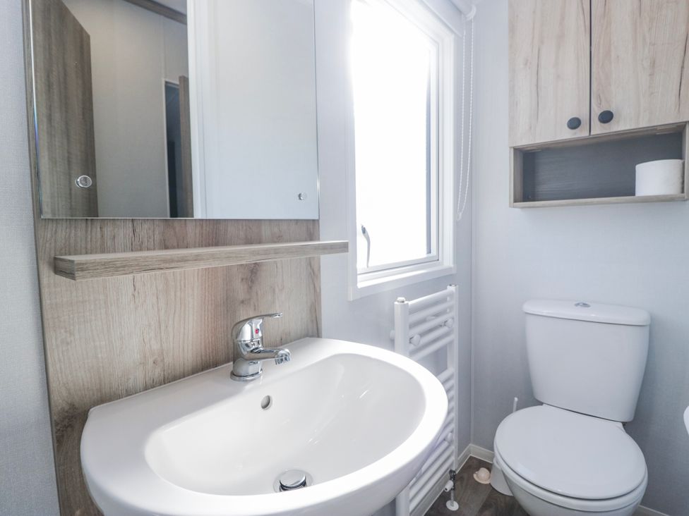 A bathroom with a sink, mirror, toilet, and window at Willerby High End Brand S6 (on Coniston) St Bees