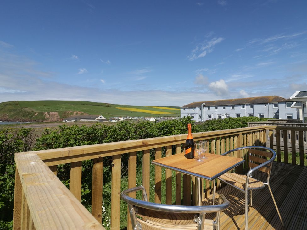 An outdoor area with a table and chairs on a deck with a view at The Swift in St Bees