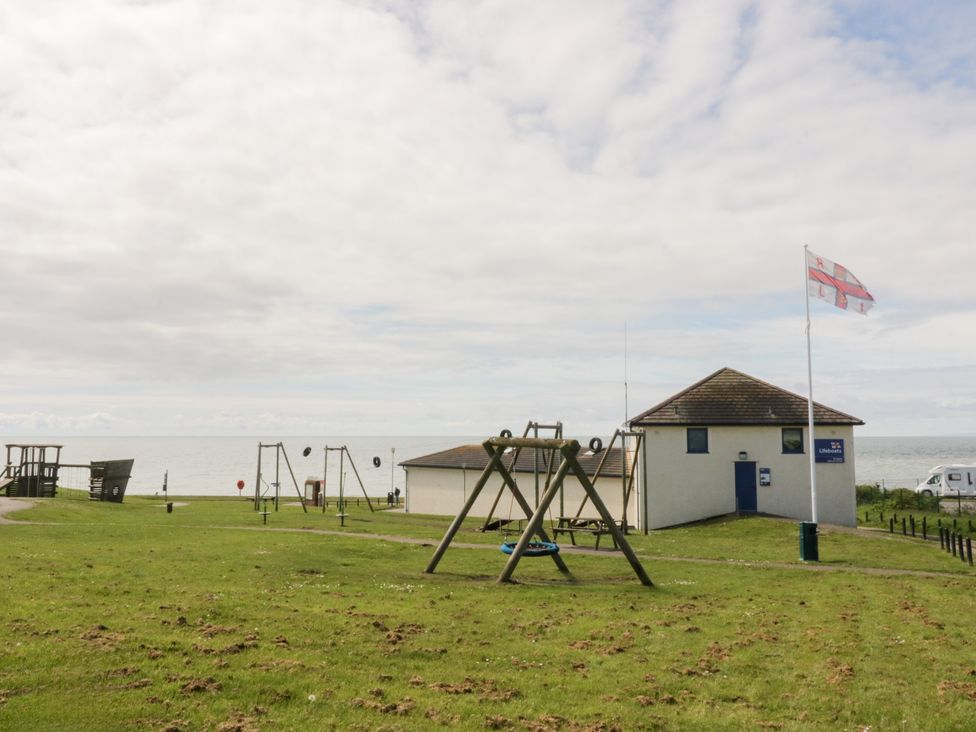 An outdoor area with playground swings and a building at The Plover in St Bees