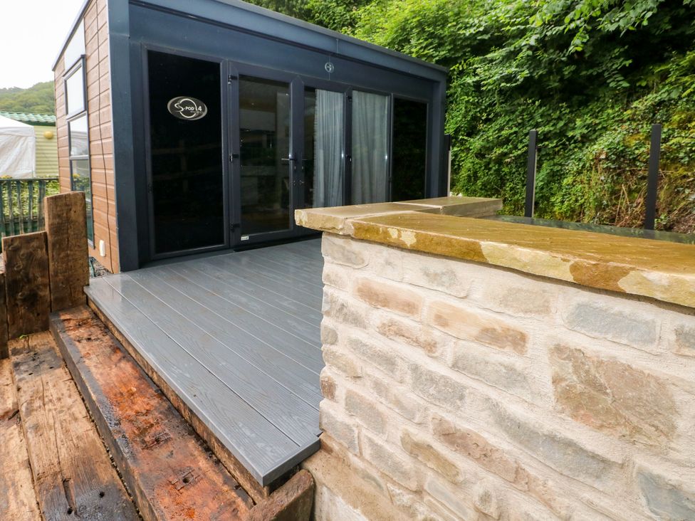 An outdoor area with a wooden deck and a stone wall at The Pod in Ferryside