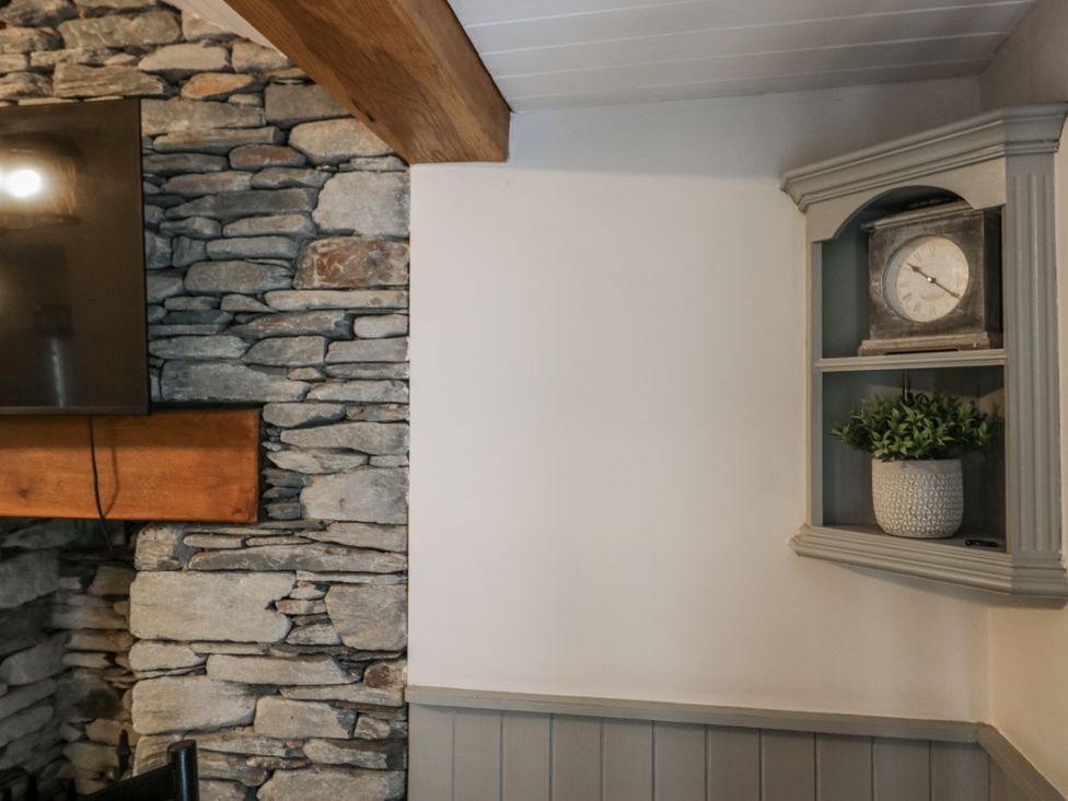 A living room with a stone wall and a clock on a shelf at The Dove Cot in Ambleside