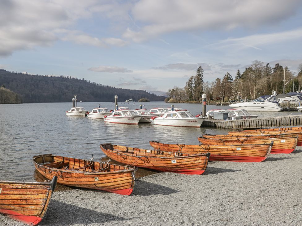 Wooden boats on a gravel shore with motorboats on water at The Dove Cot in Ambleside