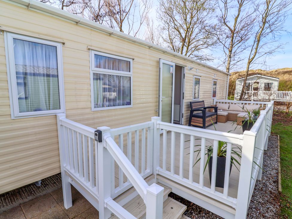 A mobile home with a deck and chairs at Presthaven Sands in Prestatyn