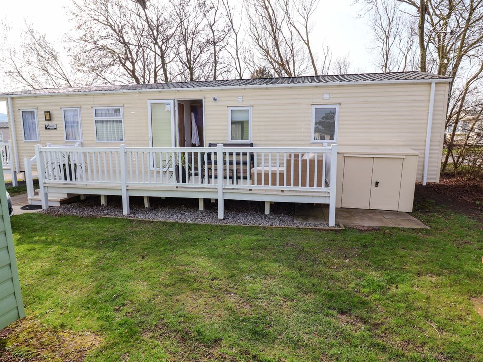 A mobile home with a deck and storage unit at Presthaven Sands in Prestatyn