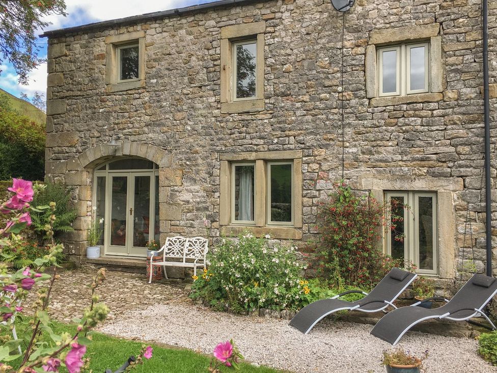 A stone cottage with windows and lounge chairs in the garden at Litton Hall Barn Cottage Skipton