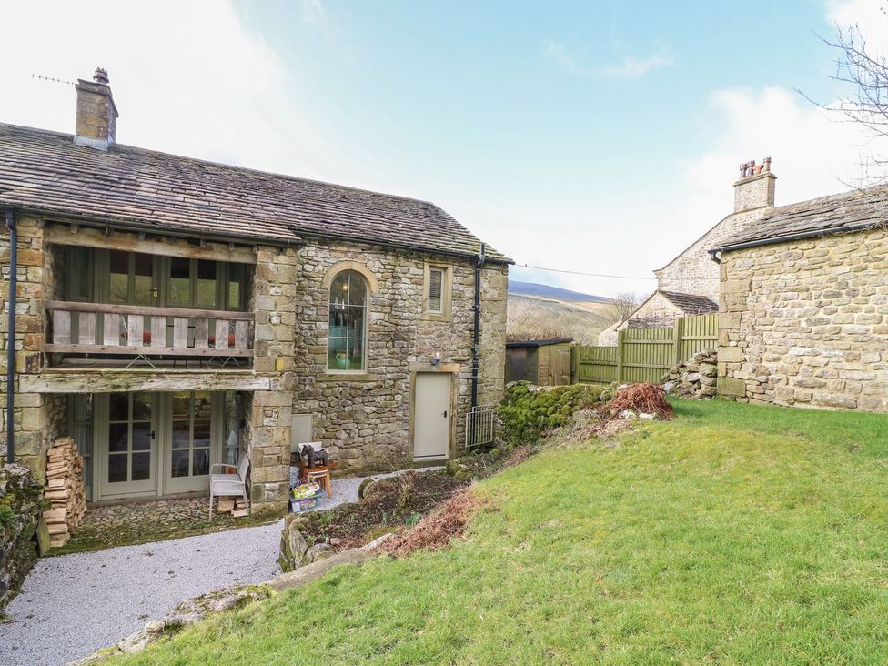 An outdoor view of a stone house with a balcony and garden at Litton Hall Barn Cottage Skipton
