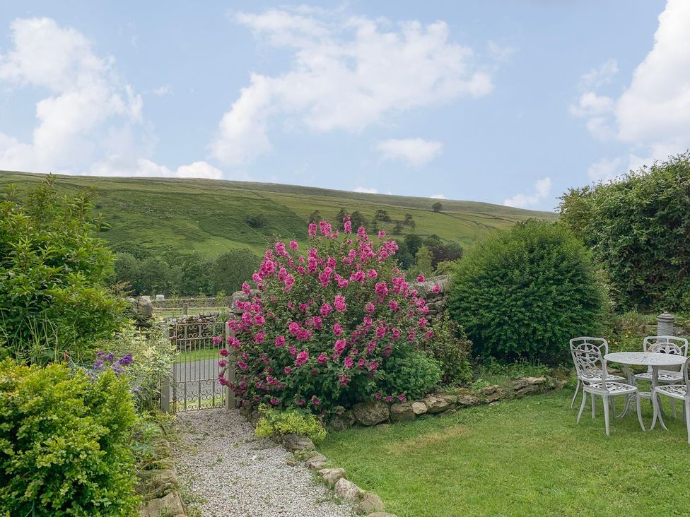 A garden with flowers, a gate, and a seating area at Litton Hall Barn Cottage, Skipton