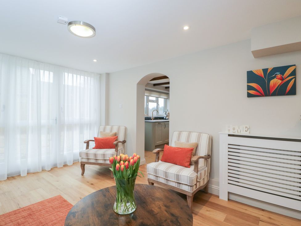 A living room with chairs, a table, and flowers at Paddock View in Stow-On-The-Wold