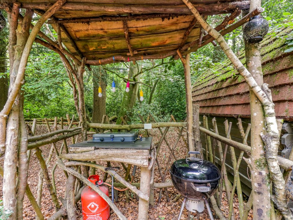 An outdoor cooking area with a wooden structure and grill at Daisy Glamping Pod in Woolton Hill