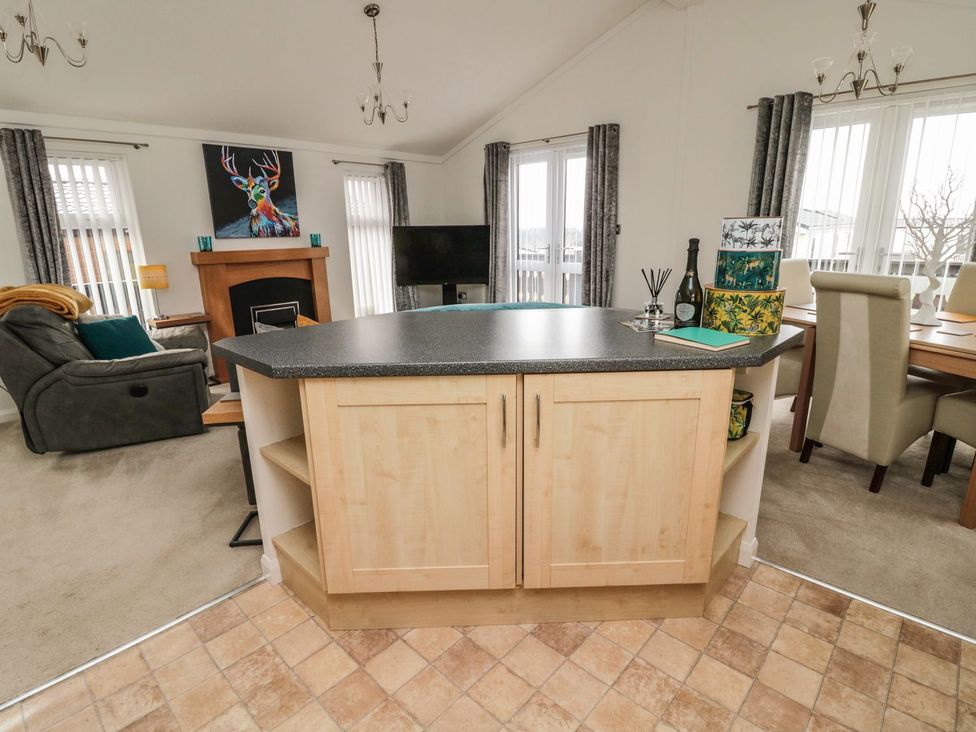 A living room with a kitchen island and television at Nevaeh Lodge Longframlington