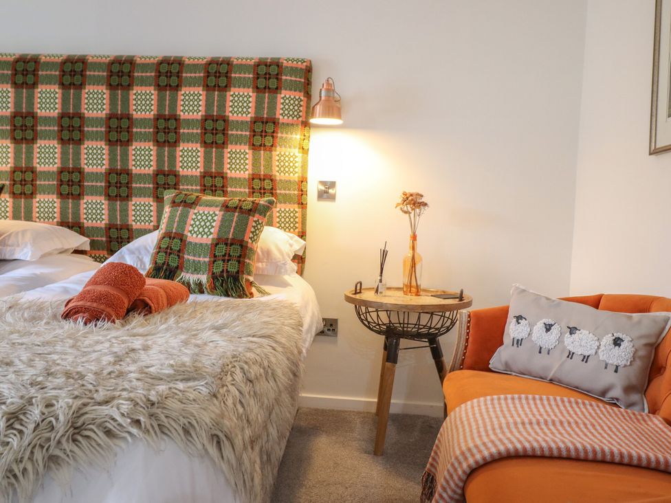 A bedroom with a bed and orange chair at The Old Cartshed | Yr Hen Gwt Cart in Abergele