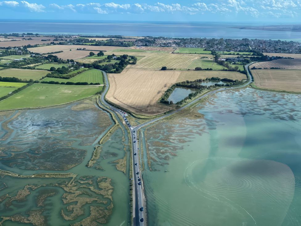 An aerial view of fields and water with a road and cars at Island Retreat in Colchester