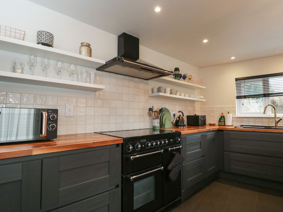 A kitchen with oven, sink, and shelves at Copper Cottage in Devizes