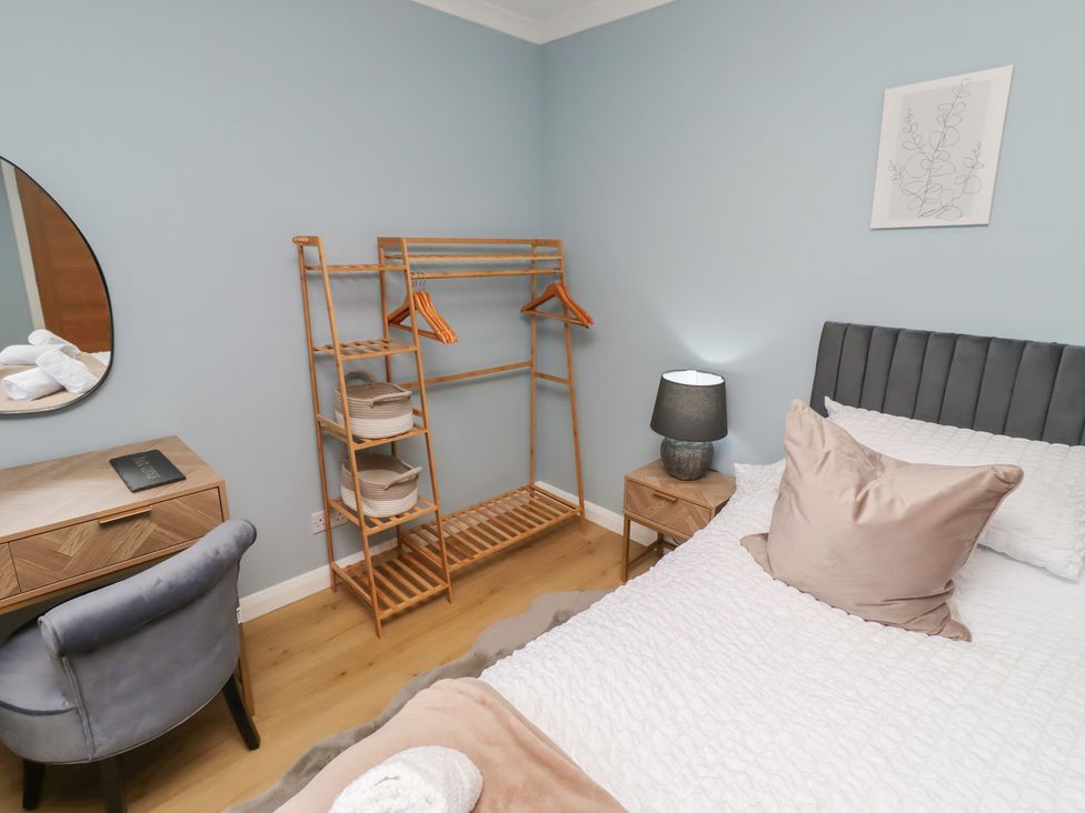 A bedroom with a bed, lamp, desk, chair, and clothes rack at Tigh-Na-Mara Retreat