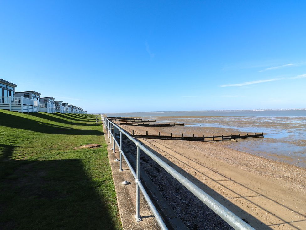 A beach with grass and beach huts at Ocean Breeze Escape in Allhallows