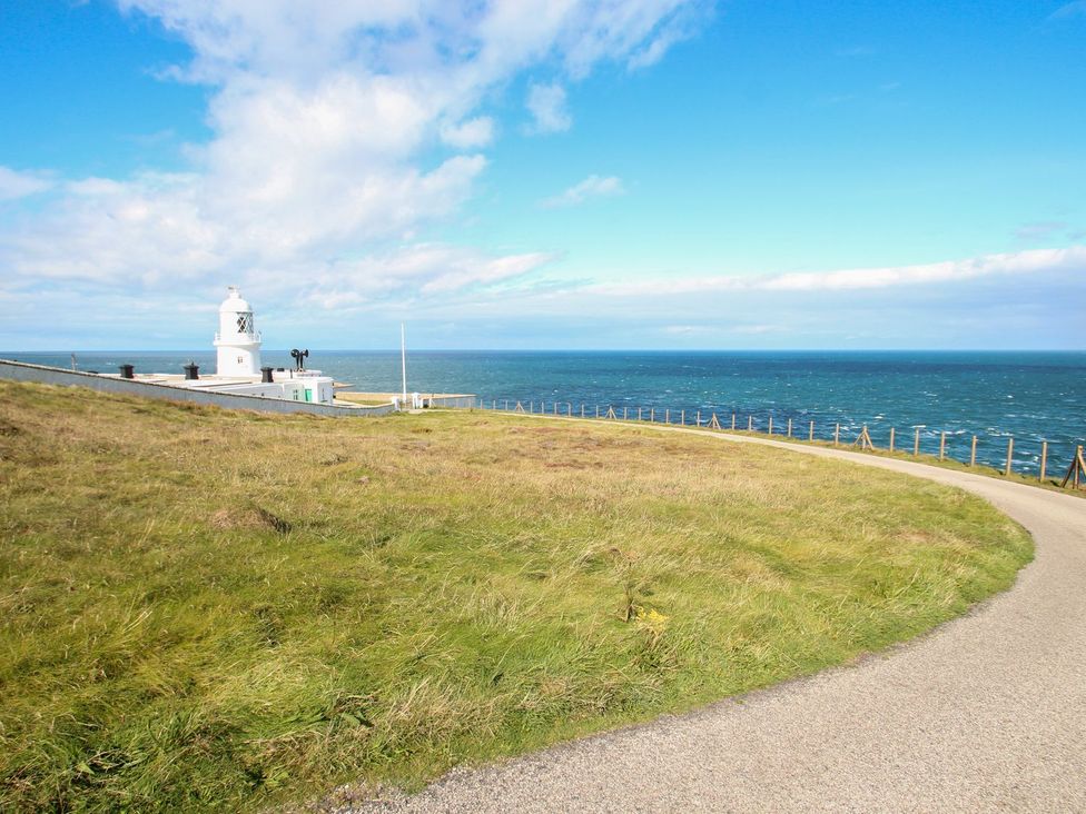 A lighthouse near the ocean with a road and grass at The Old Studio in Penzance