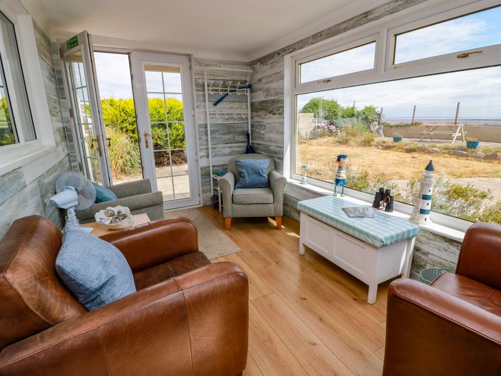 A conservatory with seating and a coffee table at Wagtail Cottage Southerness
