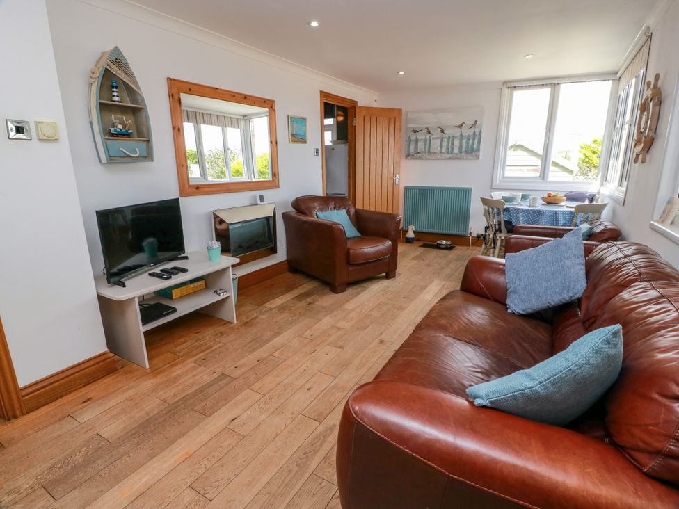 A living room with a sofa, armchair, table, and TV at Wagtail Cottage in Southerness