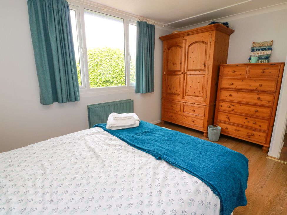 A bedroom with a bed and two wooden furniture pieces at Wagtail Cottage in Southerness