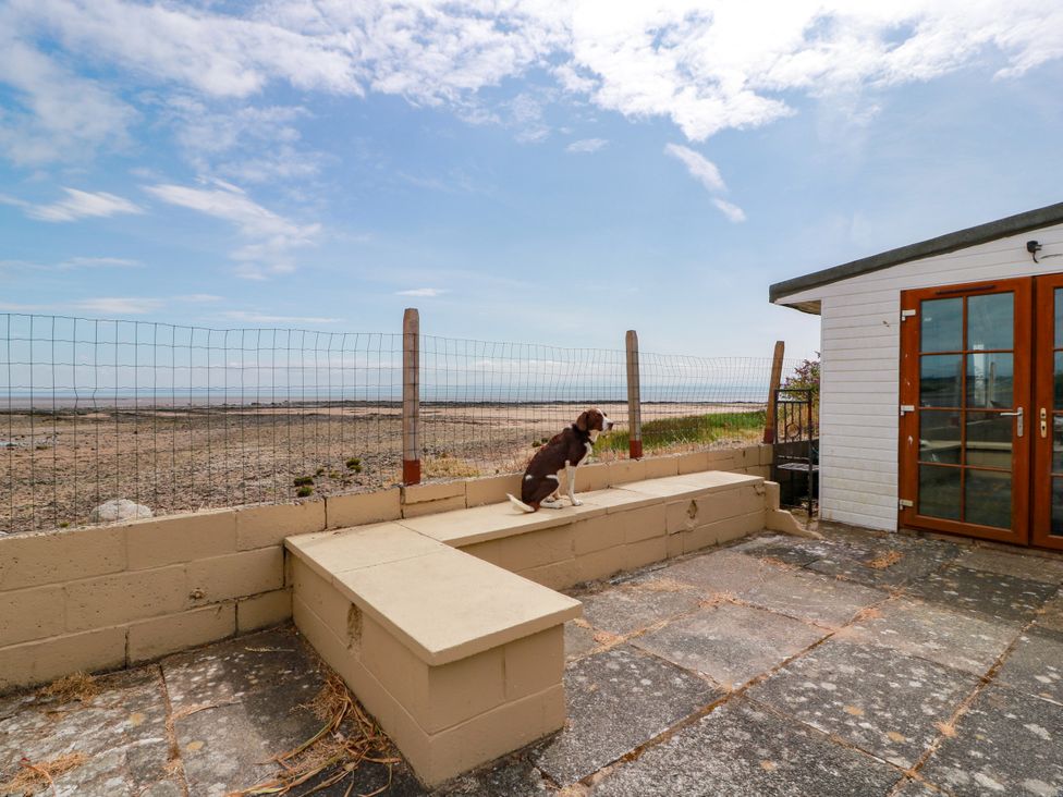 A patio area with a dog sitting near a building at Wagtail Cottage in Southerness