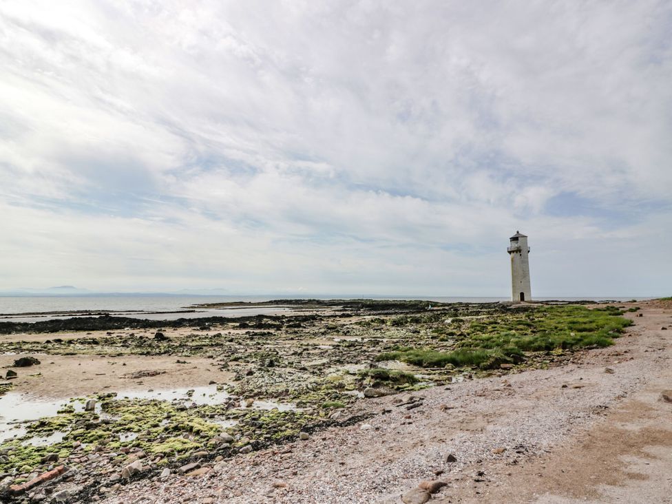 A lighthouse on the shore with rocks and grass at Wagtail Cottage Southerness