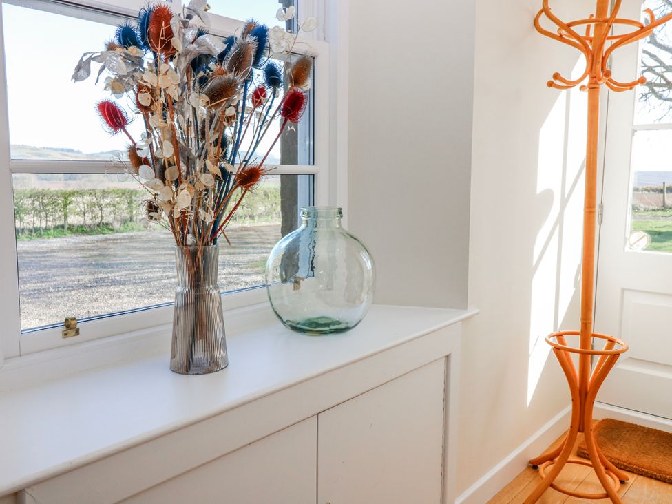 A hallway with a vase of dried flowers and a coat rack at Meadowgreen Farmhouse Forfar