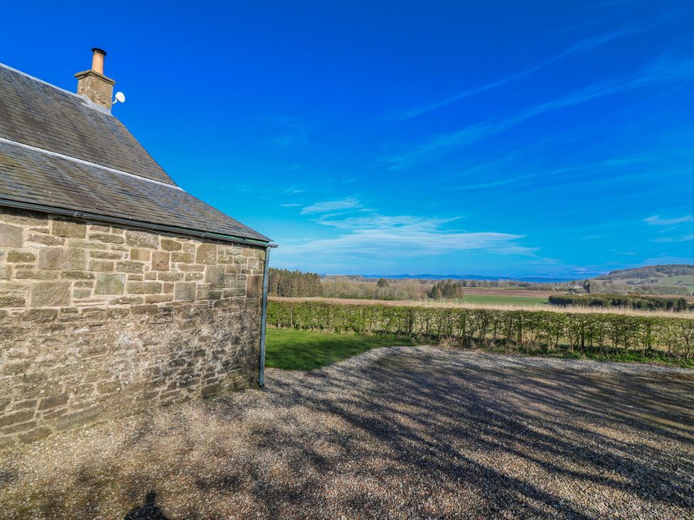 A house with a gravel area and trees in the background at Meadowgreen Farmhouse in Forfar