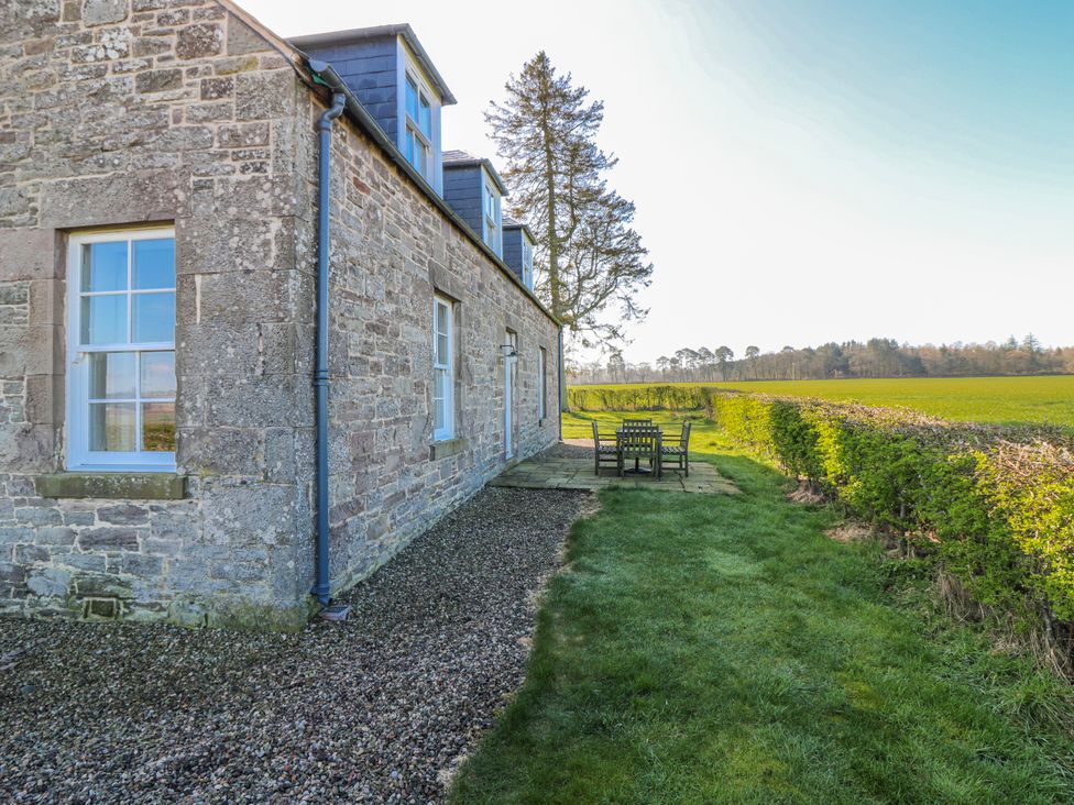 An outdoor area with a stone wall, table, and chairs at Meadowgreen Farmhouse in Forfar