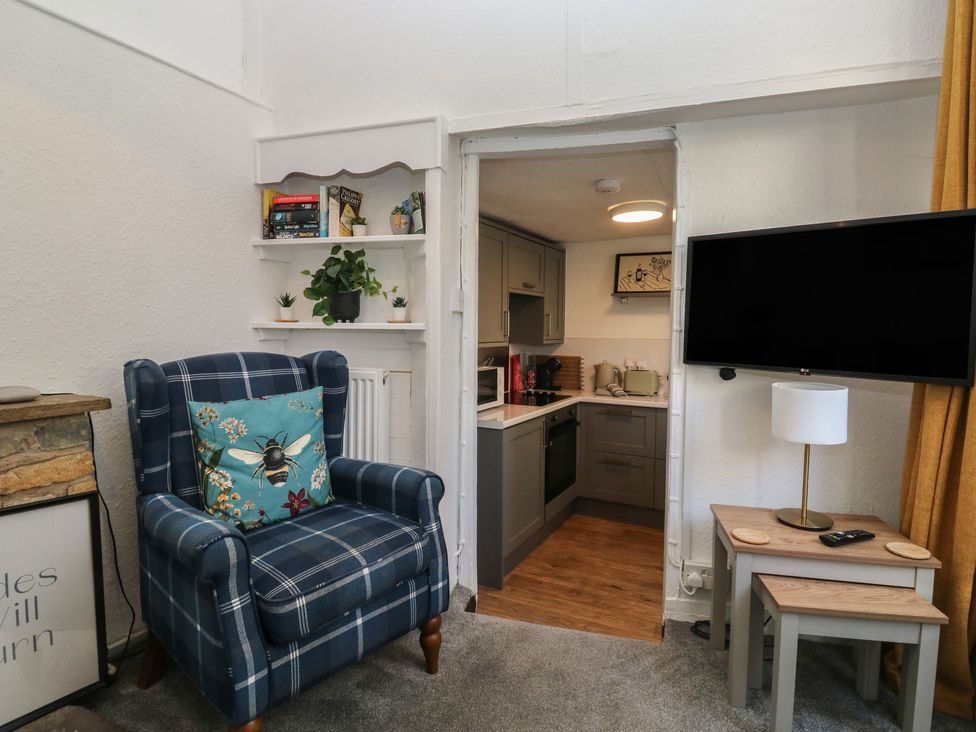 A living room with an armchair and a view of the kitchen at The Cottage in Budleigh Salterton