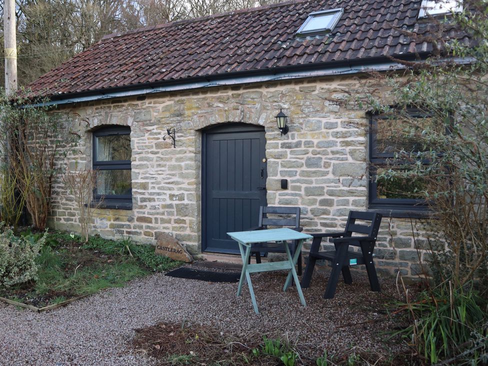 A stone cottage with a door and outdoor seating at Castle Rag in Parkend