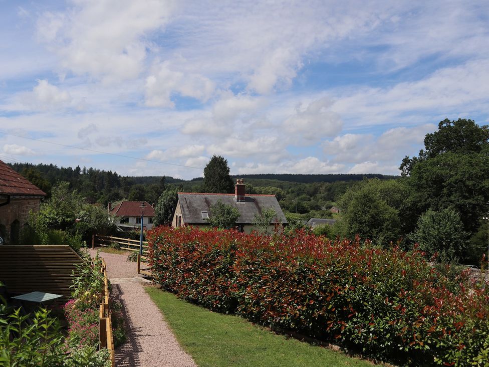A pathway leading through hedges with houses and trees at Castle Rag in Parkend