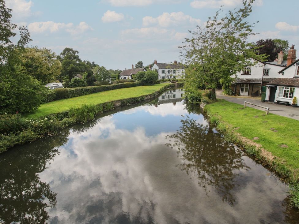 A river reflecting clouds near houses and trees at Tulip in Eardisland