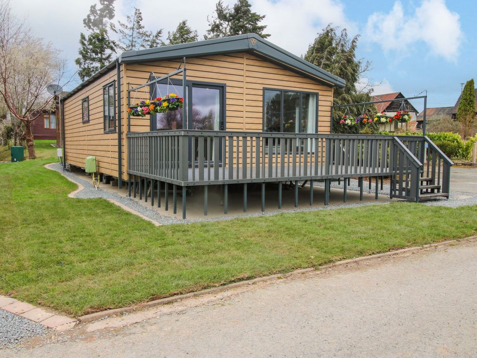 A cabin with a deck and hanging plants at Tulip in Eardisland