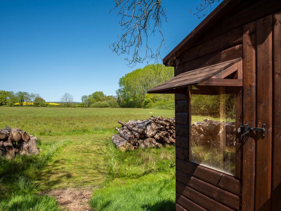 A wooden cabin and stacked logs in an outdoor area at Poppy in Eardisland