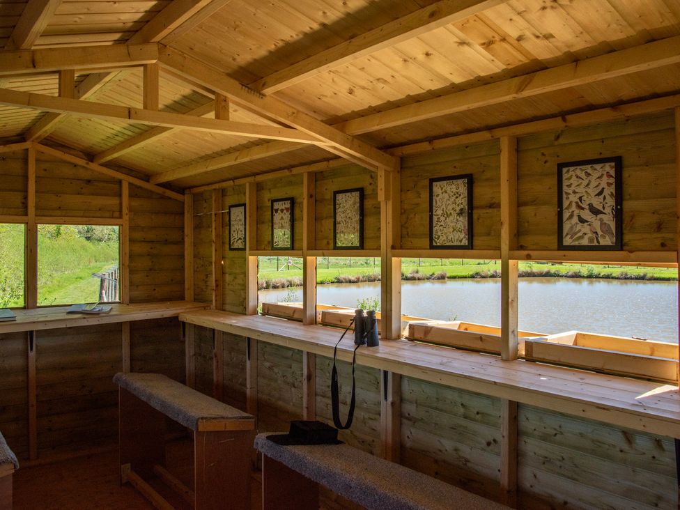 A wooden cabin with tables and benches overlooking a pond at Poppy in Eardisland