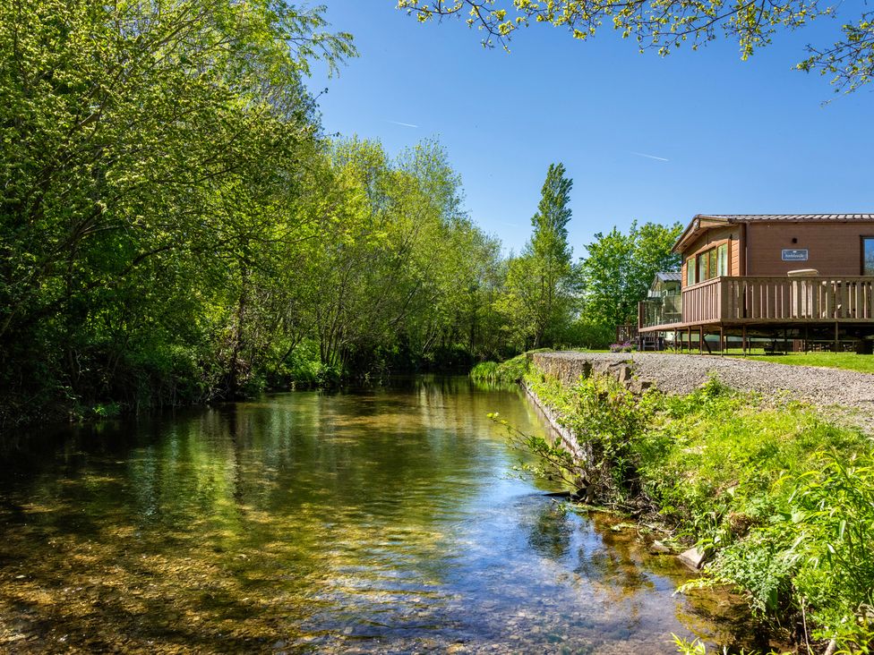 A river with trees and a cabin with a deck at Poppy in Eardisland