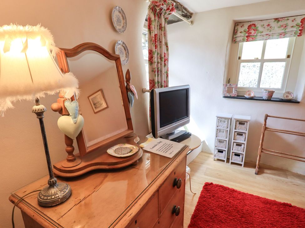 A bedroom with a lamp, mirror, television, and storage unit at Beckside Studio in Penrith