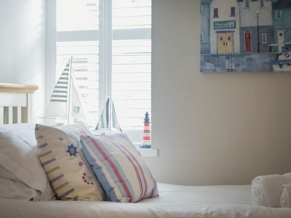 A bedroom with pillows on a bed and sailboat models on a window sill at Juniper Cottage