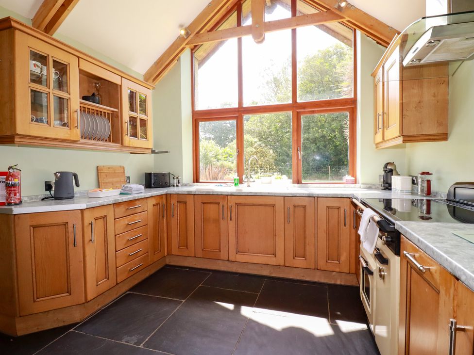 A kitchen with wooden cabinets and large windows at Little Trethellan Trethellan near Lanner
