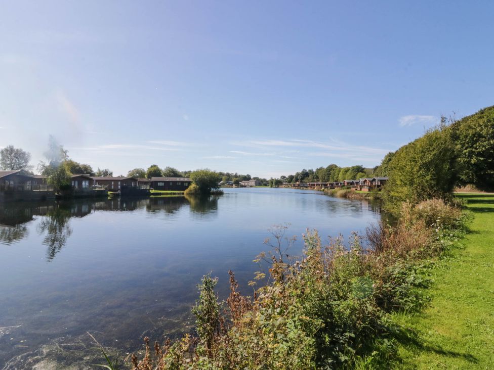 A lake with cabins along the shore at South Lakeland Lodge. No. 46 Gressingham near Carnforth