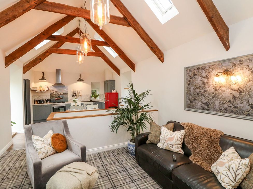 A living room with a sofa and chair leading to an open kitchen at The Old Byre in Falmouth