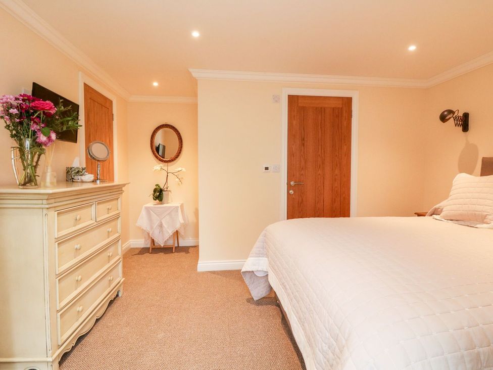 A bedroom with a bed, dresser, and mirror at The Old Byre in Falmouth