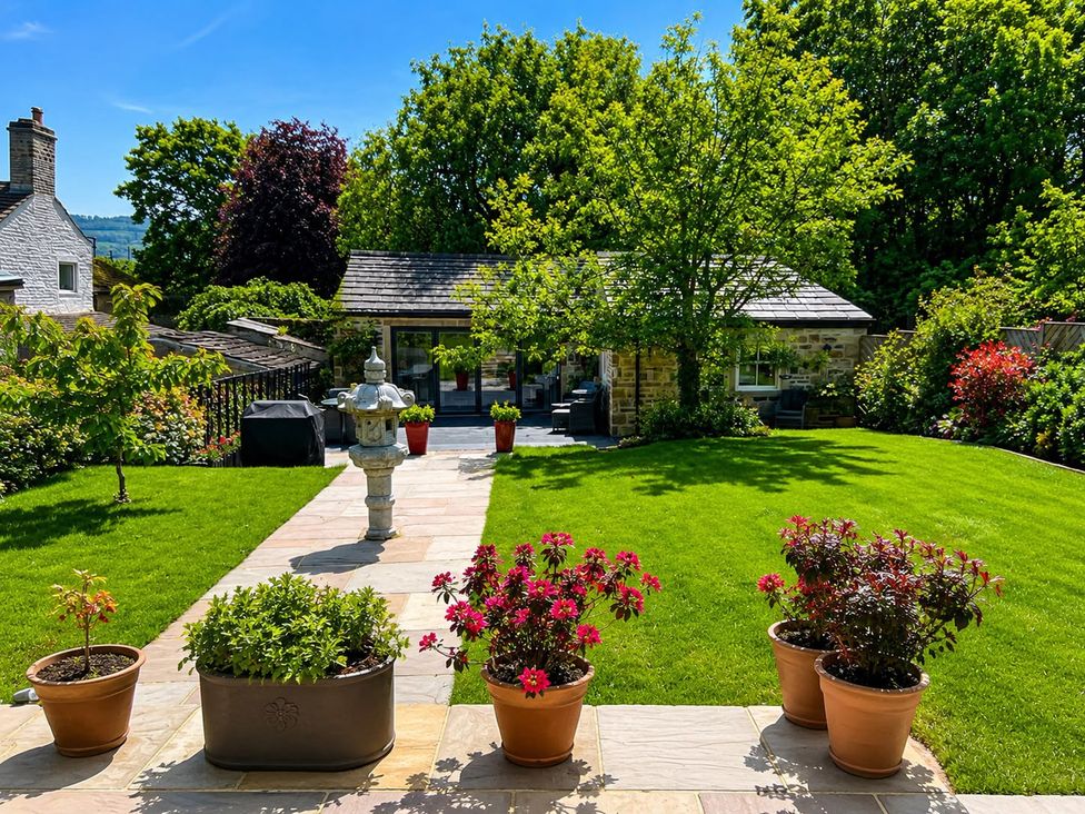 A garden with grass, flower pots, and a house at The Summerhouse in Kildwick