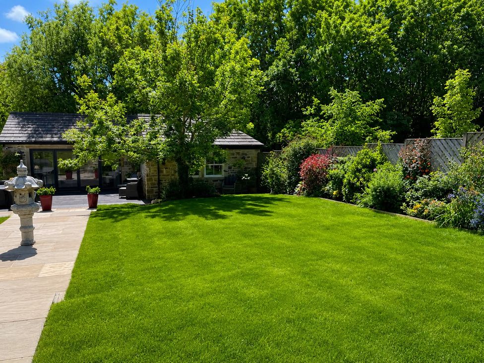 A garden with grass, plants, and a shed at The Summerhouse in Kildwick