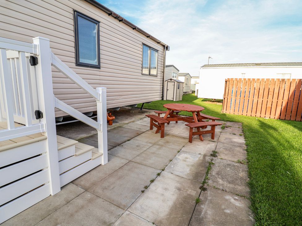 An outdoor area with a caravan, table, and benches at Chappie's Caravan 2.0 in Rhyl