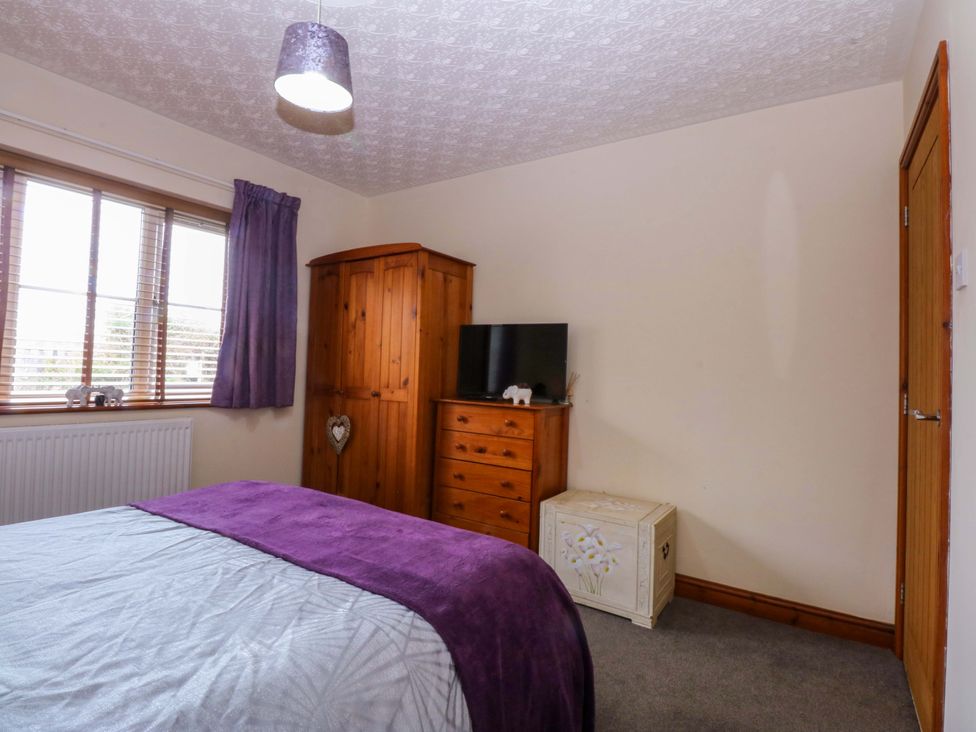 A bedroom with a bed, wardrobe, television and chest of drawers at 36 Cae Rhos in Holyhead