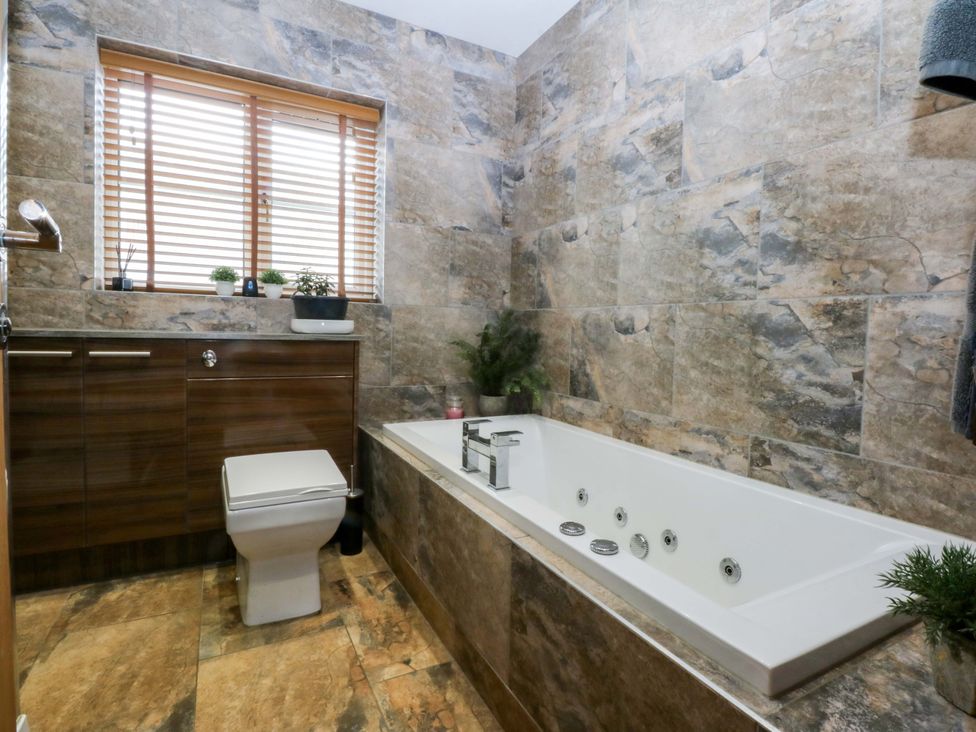 A bathroom with a bathtub, toilet, and cabinet at 36 Cae Rhos in Holyhead