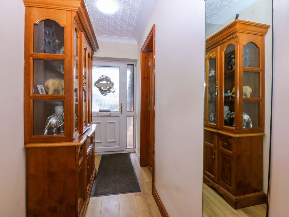A hallway with a display cabinet and door at 36 Cae Rhos in Holyhead